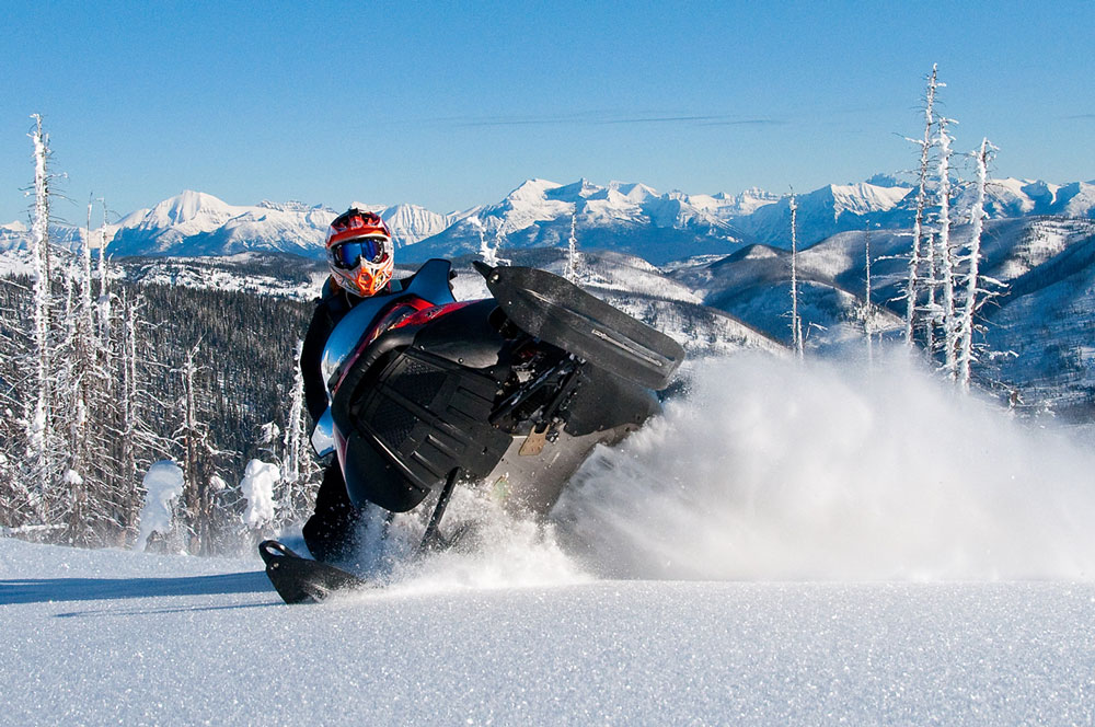 A snowmobiler making a sharp turn, kicking up snow in a mountainous landscape.