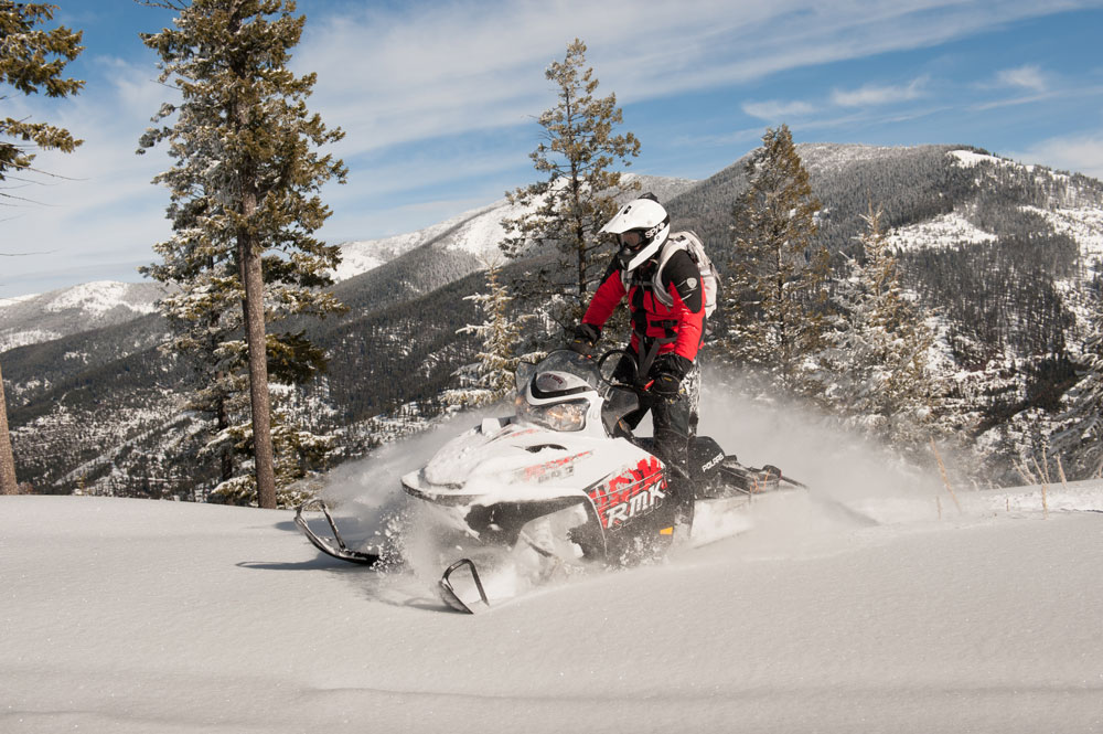 Snowmobiler carving through fresh powder in a mountainous forest.