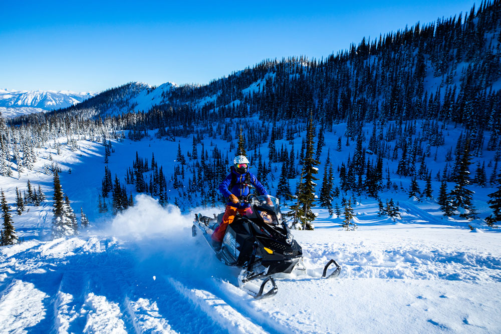 Rider on a snowmobile navigating a steep trail in a scenic winter landscape.